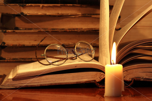 Closeup of candle with burning flame on background with old books and spectacles, stock photo