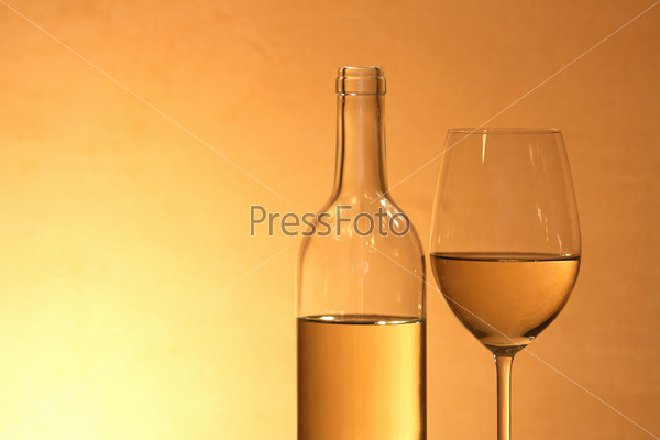 Wineglass near bottle of white wine on red-yellow background with copy space