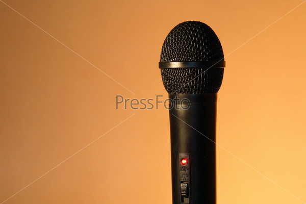 A modern black handheld ball head microphone on ginger background with copy space, stock photo