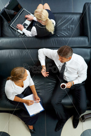 Above angle of man and woman sitting on sofa and planning work while secretary typing on background