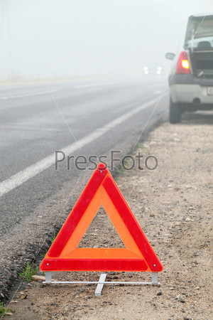 The image of emergency stop sign under the foreground and part of blurred broken car under background. Focus is under the sign.