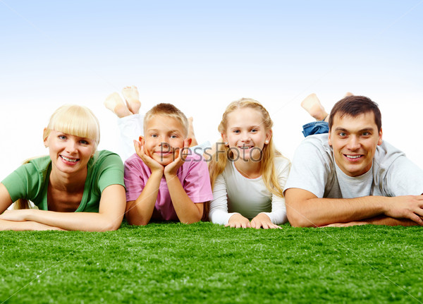 Portrait of happy family lying on green lawn and looking at camera
