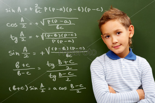 Portrait of smart schoolchild by the blackboard with sums on it looking at camera