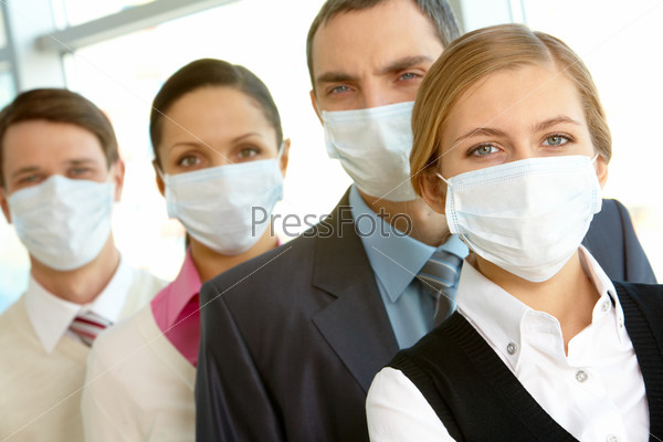 Pretty female in protective mask looking at camera on background of business people