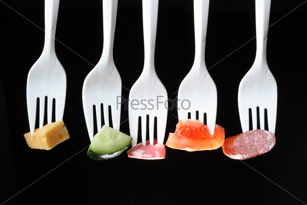 Five white plastic forks in a row with various food on a black background