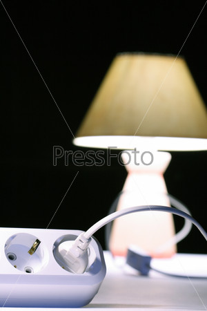 Closeup of multiple socket and plug om background with luminous table lamp