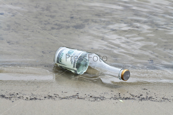 One hundred dollars note inside glass bottle lying in water on the river bank, stock photo