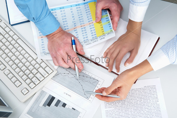 Close-up of human hands pointing at some graphs and tables with a pen, stock photo