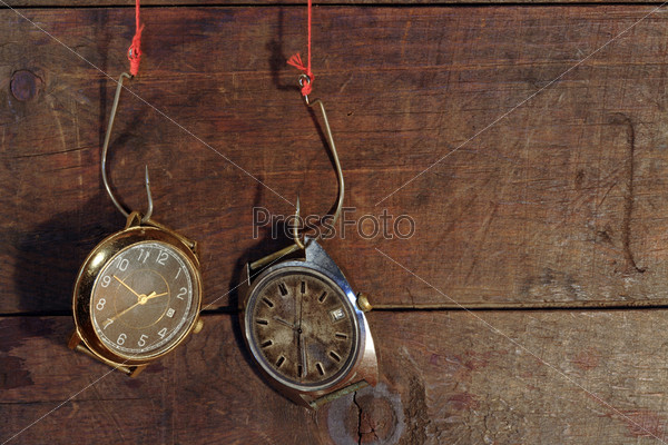 Two old watches hanging on fish hooks on wooden background