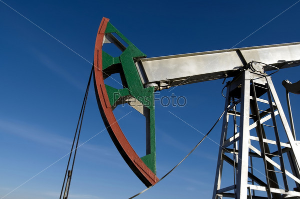 Green with red stripe on the silver lever oil pump rocking against the blue sky, stock photo