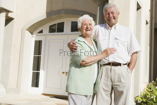 Senior couple standing outside front door of house