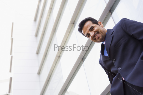 Businessman standing outside modern office building, stock photo