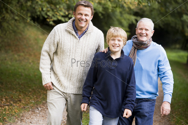 Grandfather walking with son and grandson along autumn path