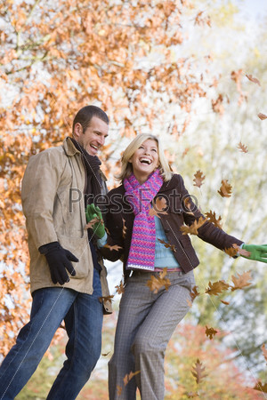 Молодая пара подбрасывает осенние листья в воздух