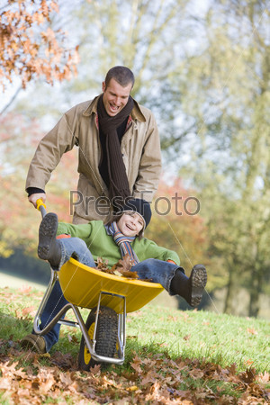 Father giving son ride in wheelbarrow through autumn leaves