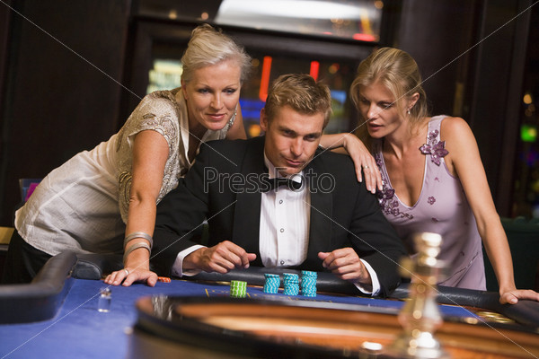 Man with glamorous women in casino at roulette table