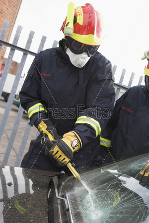 Firefighters breaking a car windscreen to help a car crash victim