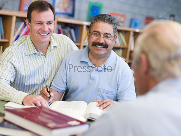 Two men sitting in library near another man with a book and notepad (selective focus)