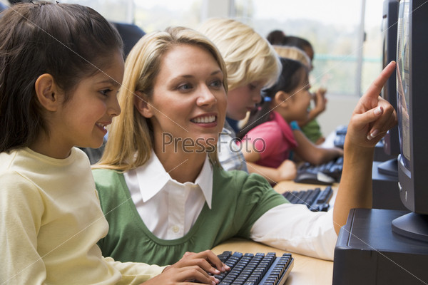 Teacher helping student at computer terminal with students in\
background (depth of field/high key)