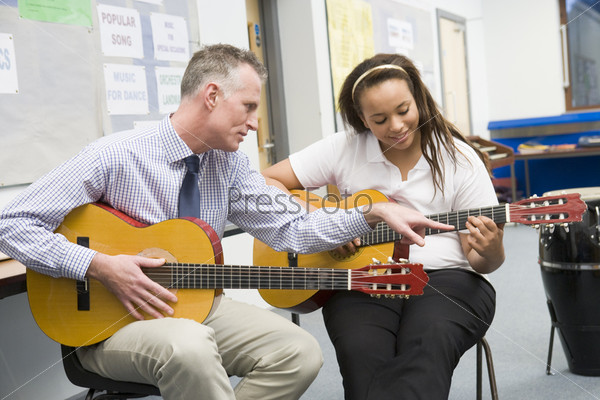 Schoolgirl and teacher playing guitar in music class
