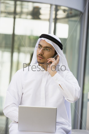Ближневосточный бизнесмен, использующий мобильный телефон и ноутбук