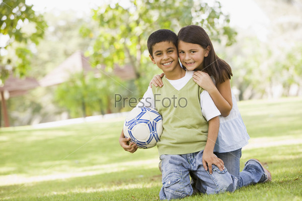 Two children playing football in park looking to camera, stock photo
