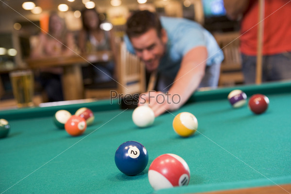 Young man playing pool in a bar (focus on pool table)