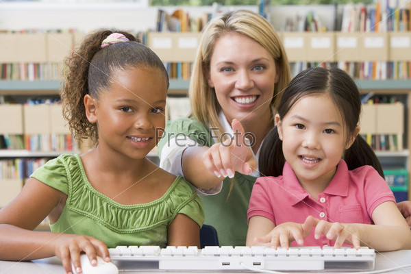 Two students in class at computer keyboard with teacher