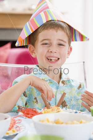Young boy at party sitting at table with food smiling
