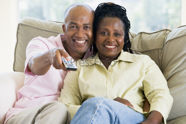 Couple relaxing in living room holding remote control and smiling
