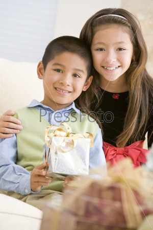 Brother And Sister Sitting On Couch Holding Christmas Gift