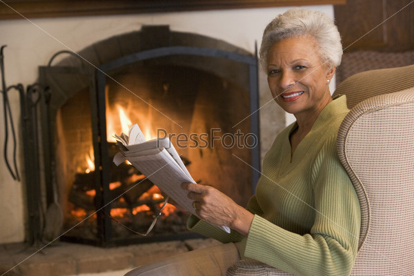 Woman sitting in living room by fireplace with newspaper smiling