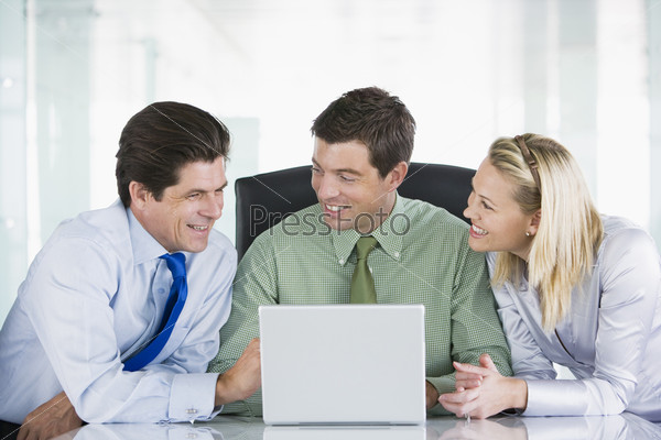 Three businesspeople in a boardroom looking at laptop\
smiling