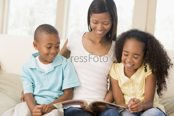Woman and two children sitting in living room reading book and smiling