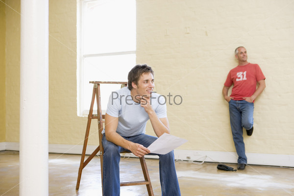 Two men with ladder in empty space one holding paper smiling