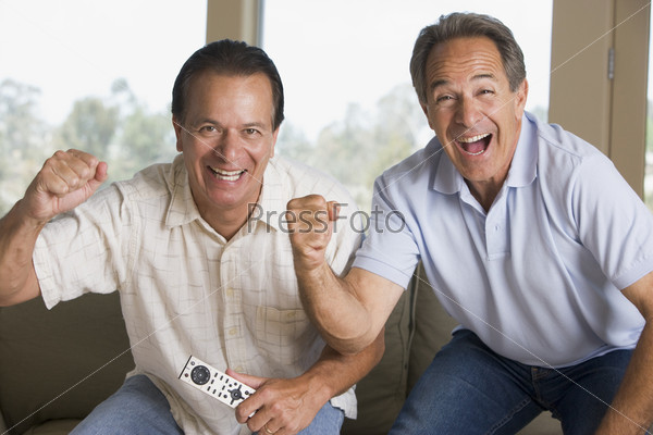 Two men in living room with remote control cheering and smiling
