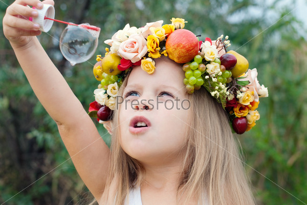 Happy Child in Summer.  Beautiful Girl with Flowers Wreath from Flowers blows Soap Bubbles. Happy Children. Healthy Kids. Spring Time.