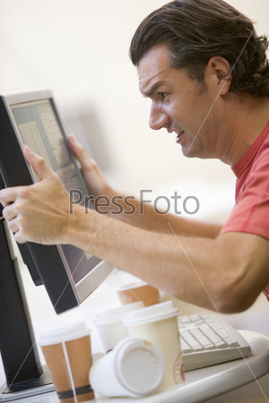 Man in computer room with many empty cups of coffee grabbing his monitor frustrated