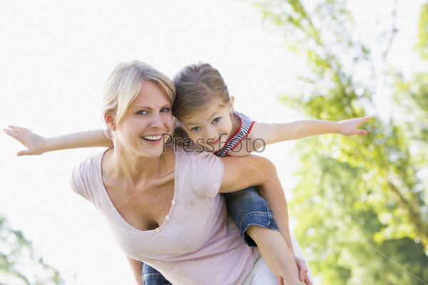 Woman giving young girl piggyback ride smiling