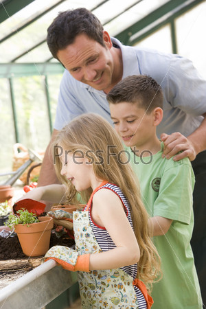 Man in greenhouse helping two young children putting soil in pot