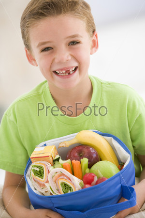 Young boy holding packed lunch in living room smiling