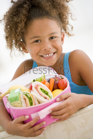 Young girl holding packed lunch in living room smiling