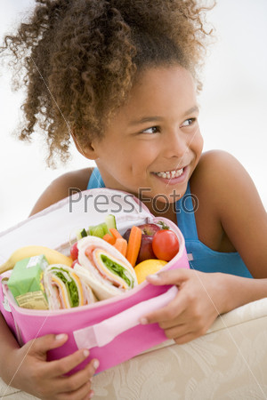 Young girl holding packed lunch in living room