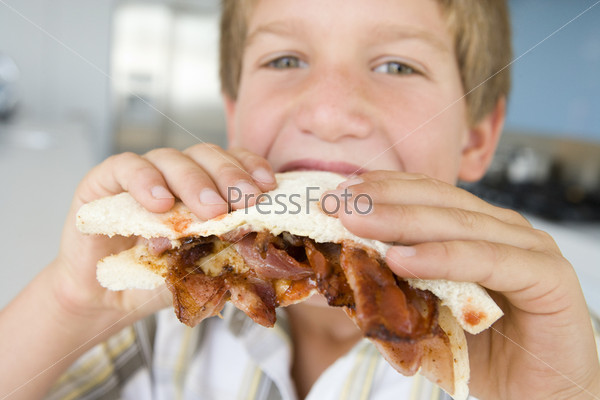Boy eating bacon sandwich at home