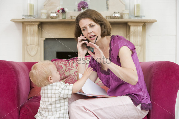Mother using telephone in living room with baby frowning