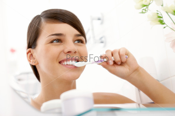 Молодая девушка чистит зубы перед зеркалом