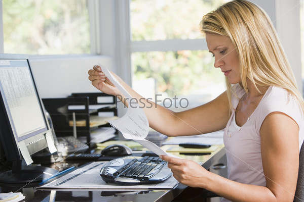 Woman in home office with computer and paperwork frowning