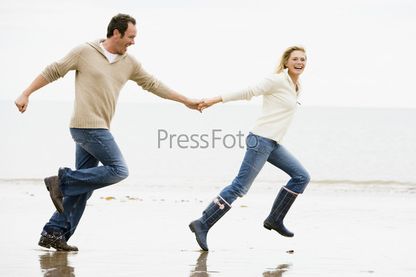 Couple running on beach holding hands smiling