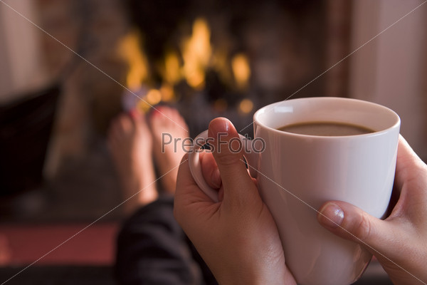 Detail of young woman holding cup of coffee by fire