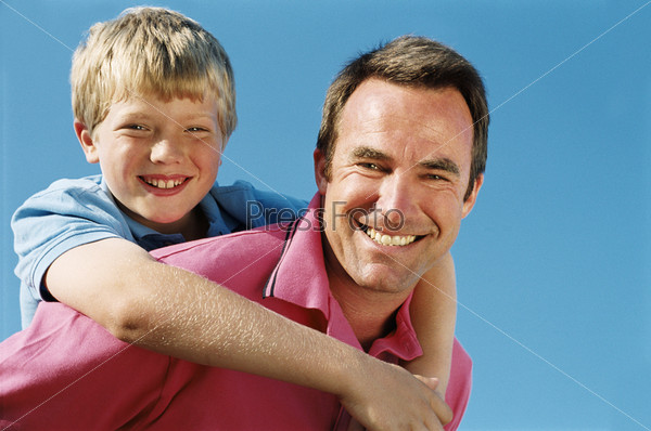 Father giving son piggyback ride outdoors smiling